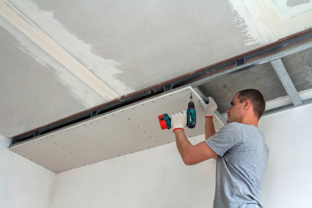 jeune homme dans les vêtements habituels et les gants de travail fixant le plafond suspendu de cloison sèche au cadre en métal utilisant le tournevis électrique sur le plafond isolé avec la feuille d’aluminium brillante. diy, faites-le vous-même co - plafond suspendu photos et images de collection